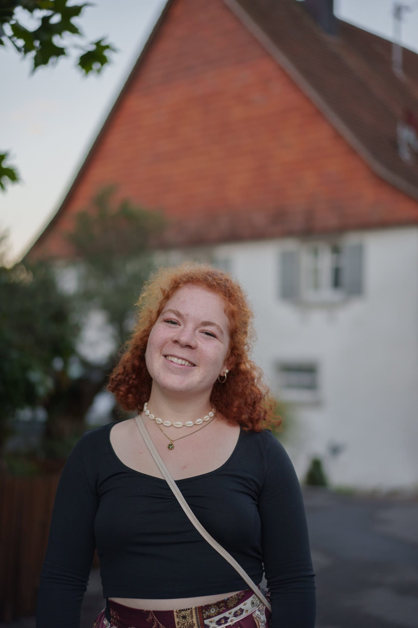 Zu sehen ist eine junge Frau, die frontal in die Kamera lacht. Das Foto ist Teil eines Portraitshooting draußen an einem Sommernachmittag.