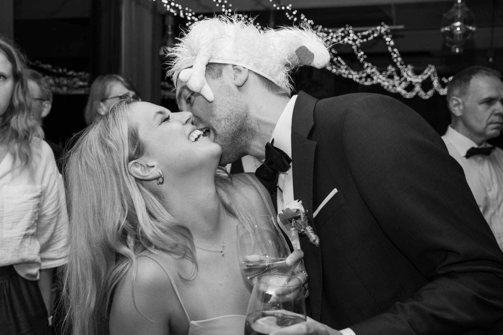 Hochzeitspaar küsst sich mit Weihnachtsmütze, festliche Stimmung, romantischer Moment bei Feier.
