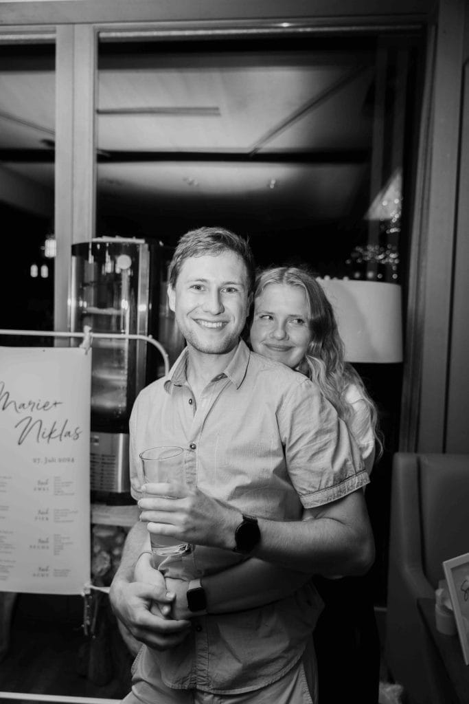 Lächelndes Paar bei Feier, festliche Atmosphäre, stilvolle Eventfotografie in Schwarz-Weiß.