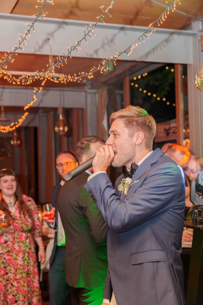 Hochzeitspaar beim Empfang, umgeben von Freunden, unter festlicher Dekoration mit Lichterketten.