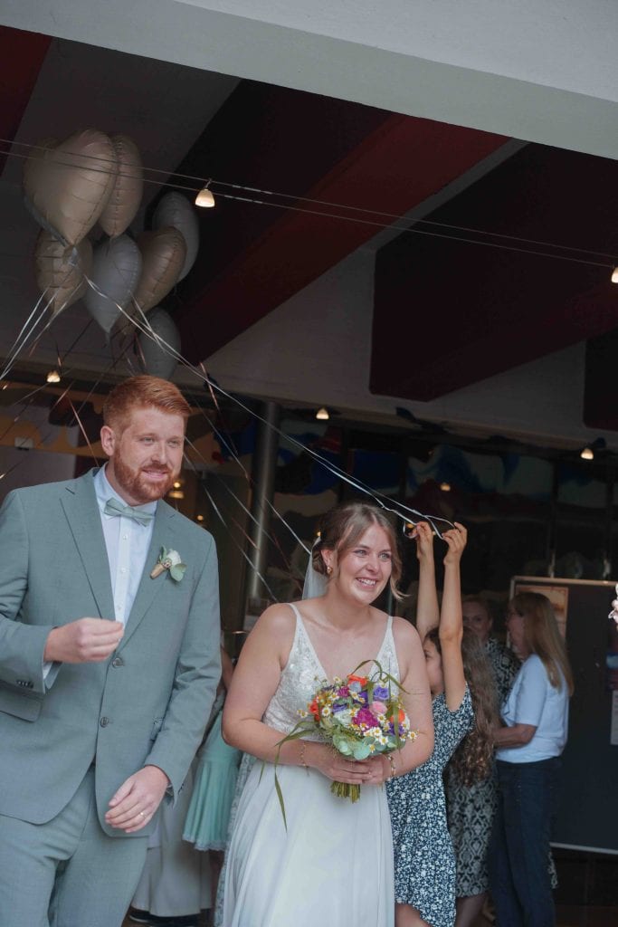 Fröhliches Hochzeitspaar bei Feier im Innenraum mit Dekoration und Gästen.
