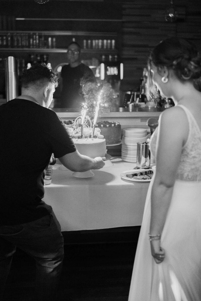 Hochzeitstorte mit Kerzen, Gäste und Feier im Hintergrund, festliche Atmosphäre.