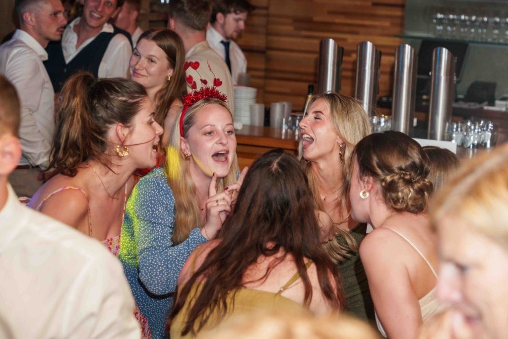 Fröhliche junge Menschen lachen und unterhalten sich bei einer Party in einer Bar, umgeben von Holzd.