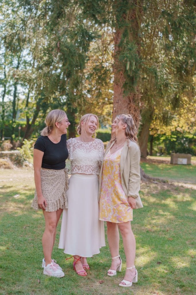 Drei lachende Frauen im Park bei Sonnenschein, freundschaftliche Atmosphäre, Natur im Hintergrund.