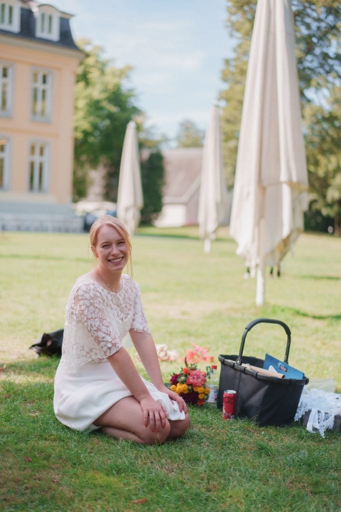 Frau sitzt lachend im Park auf dem Rasen, umgeben von Sonnenschirmen und Natur, bei einem entspannte.