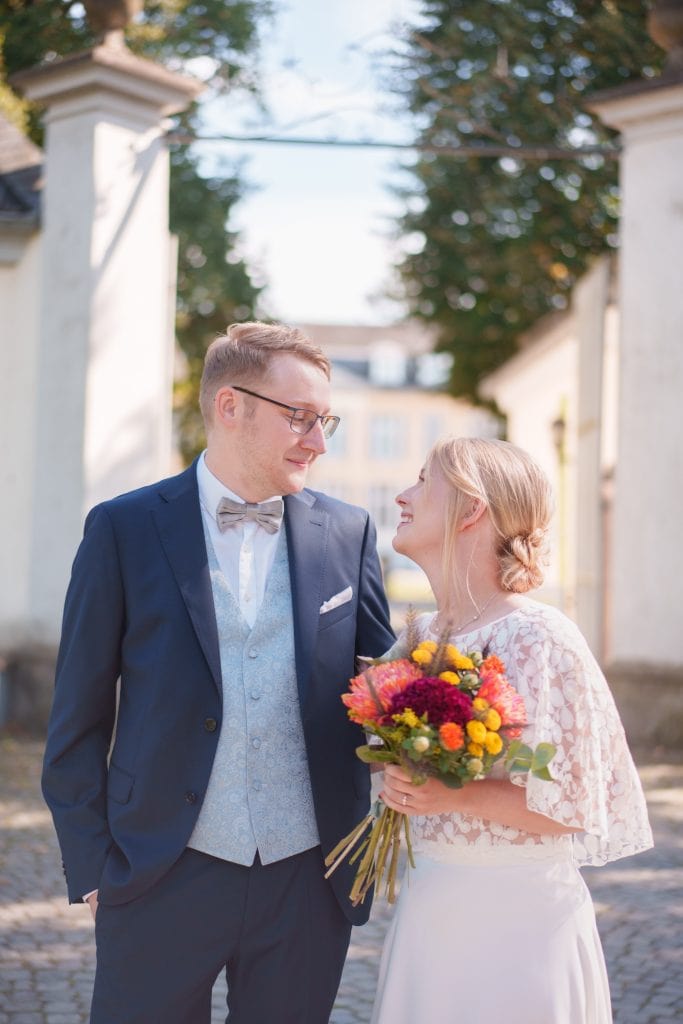 Glückliches Brautpaar bei der Hochzeit im Freien, lächelnd und mit Blumen.