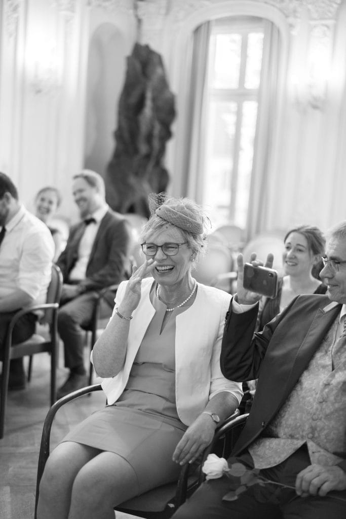 Menschen lachen und fotografieren bei einer Hochzeit im stilvollen Raum.