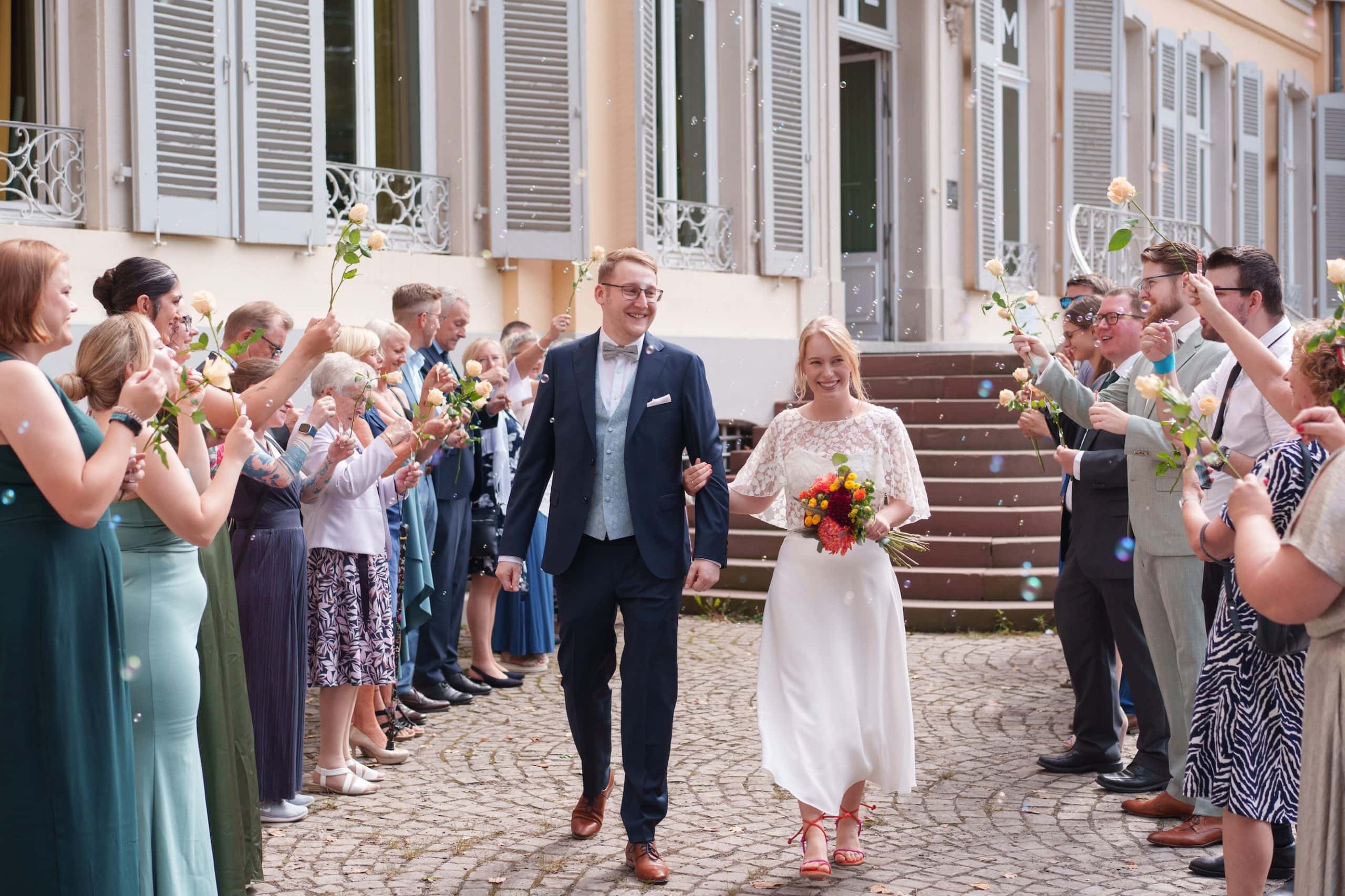 Fröhliches Hochzeitspaar mit Freunden und Familie bei der Feier im Freien.